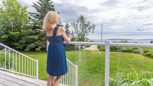 A woman in a blue dress standing on a wooden deck with a railing, overlooking a grassy area with trees and a body of water in the distance. - Adventure Awaits at Salt & Tide Ocean Retreat (Hubbards)