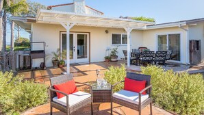 A patio with wicker furniture and a glass table, surrounded by greenery. - Views, Ocean/Mountain, Hot Tub, AC, Walk to Mesa Village, Gated Yard (Santa Barbara)