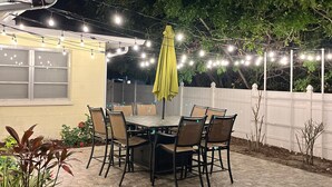 An outdoor patio with a table and chairs, surrounded by a white fence and string lights. - Get To the Beach!  Only 5 miles to Siesta Key Beach! (Sarasota)