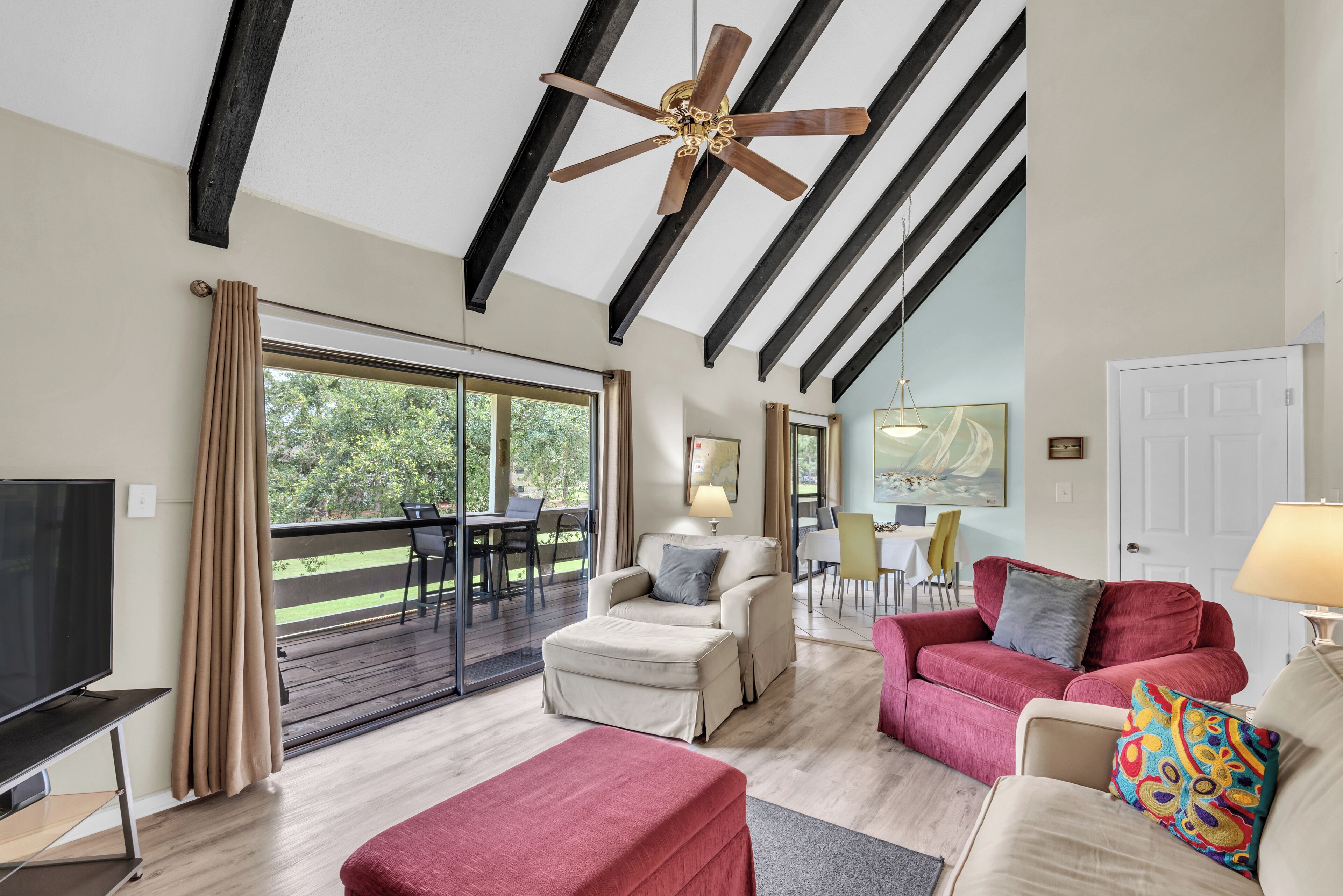 A spacious living room with a large TV, comfortable seating, a ceiling fan, and a sliding glass door leading to an outdoor area.