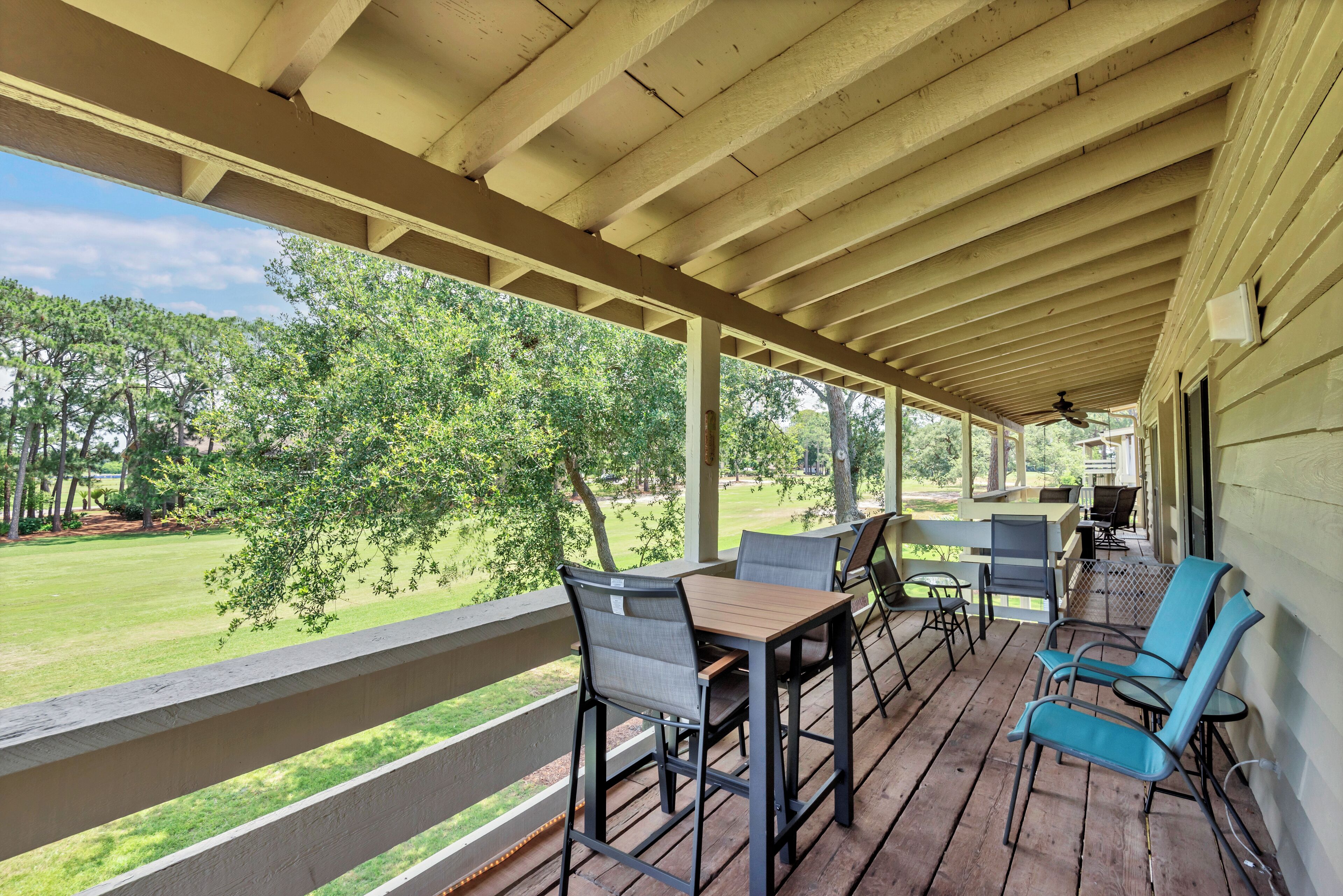 A covered porch with a table and chairs, a view of a green lawn and trees, and a ceiling fan.