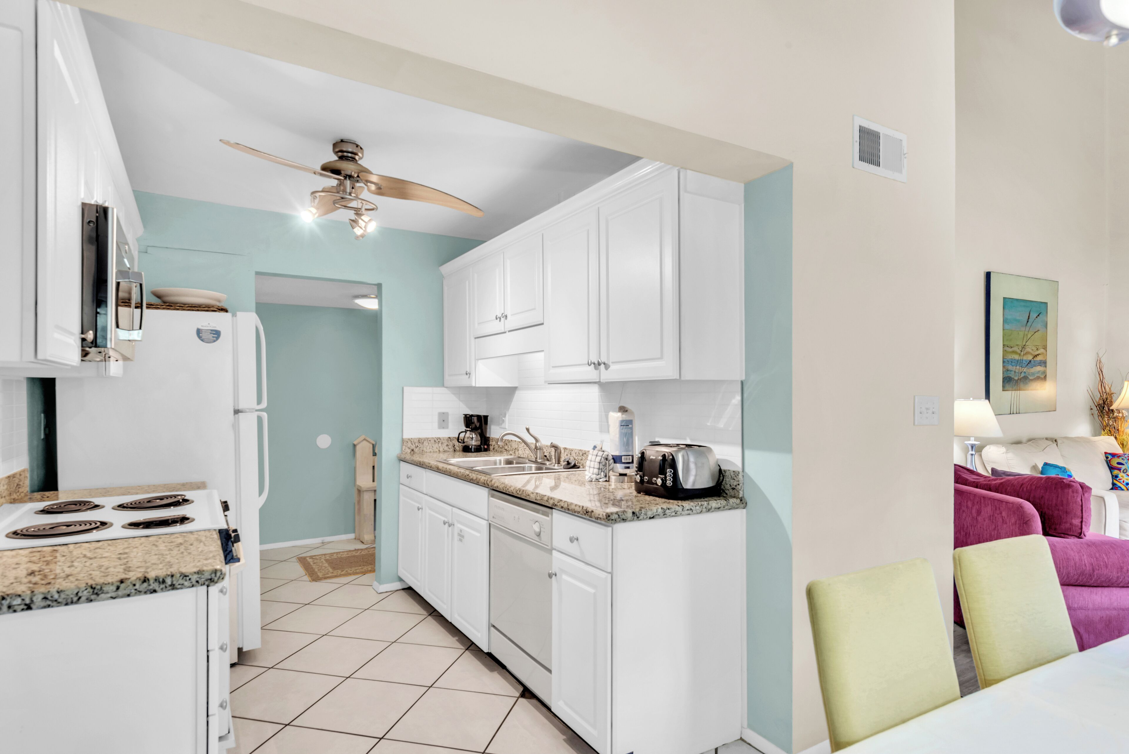 A modern kitchen with white cabinets, a granite countertop, and a ceiling fan.