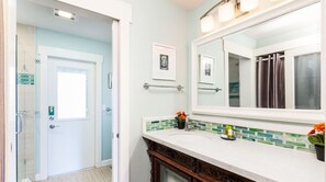 A bathroom with a white door, a glass shower enclosure, a vanity with a mirror, and a tiled backsplash. - Remodeled Beach House w/Roof Top & Deck Ocean View (Aptos)