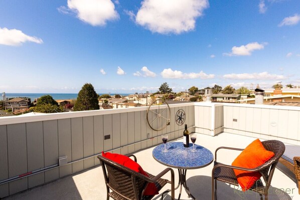 A rooftop terrace with a round table and wicker chairs, overlooking a coastal cityscape. - Remodeled Beach House w/Roof Top & Deck Ocean View (Aptos)