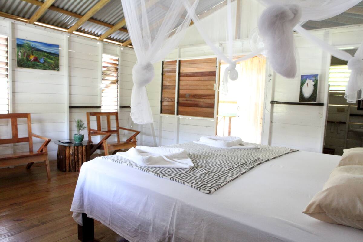 A bedroom with a bed, a chair, a small table, and a painting on the wall.