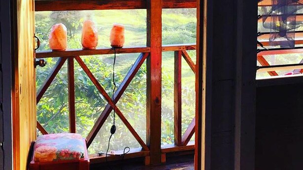 Una terraza de madera con barandilla, un taburete pequeño y vistas al verdor exterior.