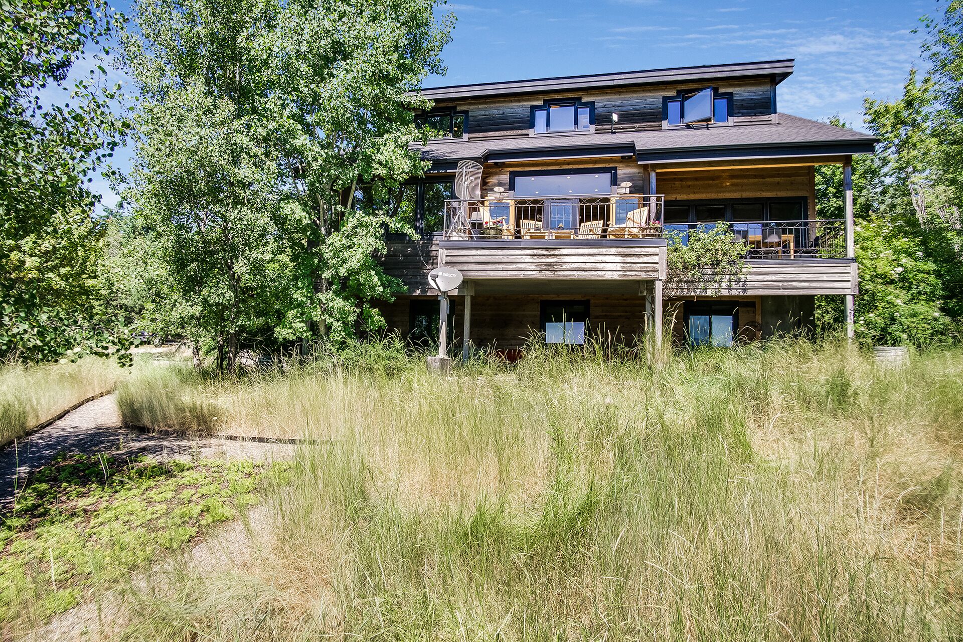 A two-story log cabin with a balcony, surrounded by tall grass and trees.