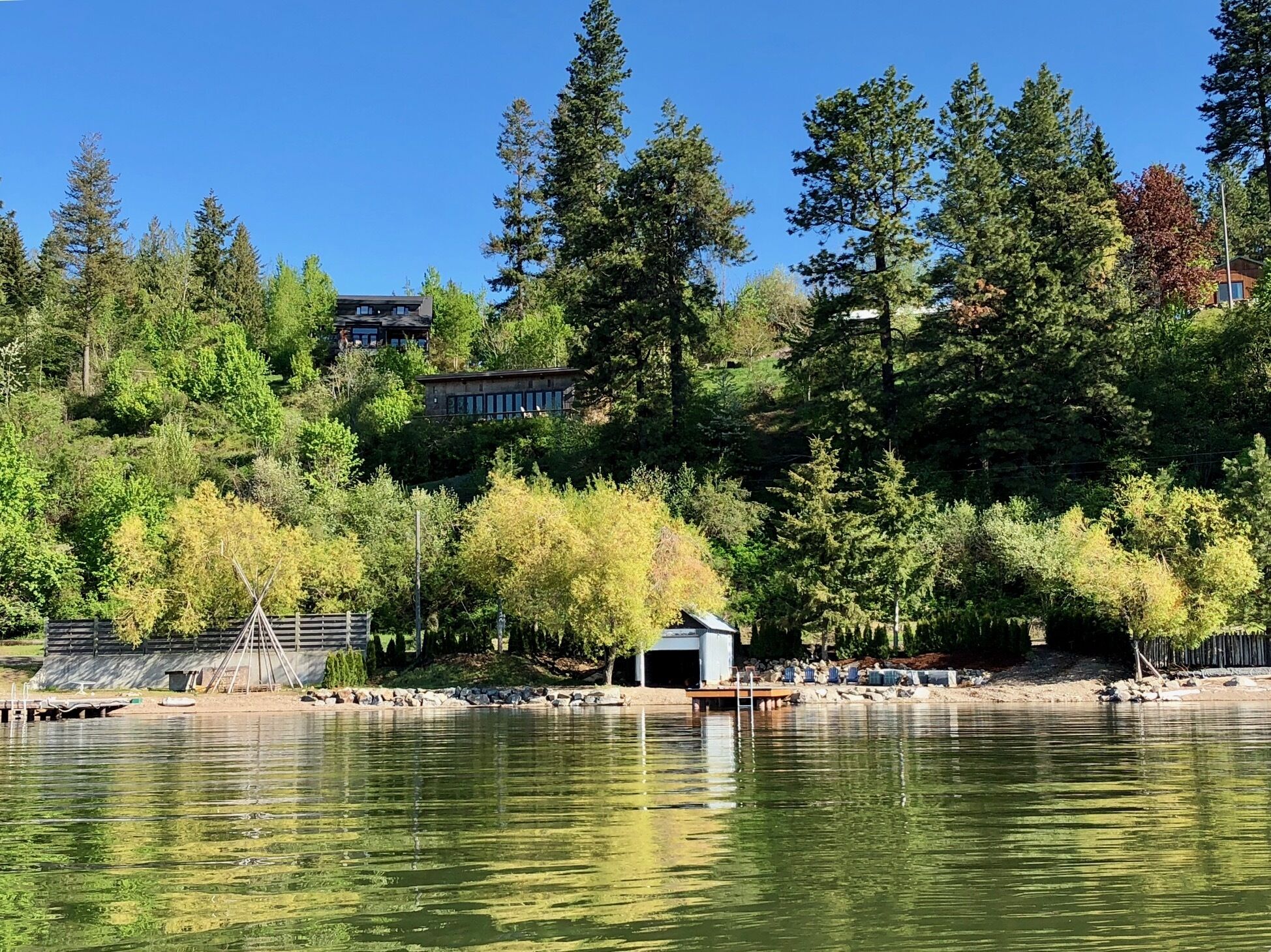 Una proprietà sul lago con un molo, una piccola casetta e una casa grande immersa in un bosco fitto.