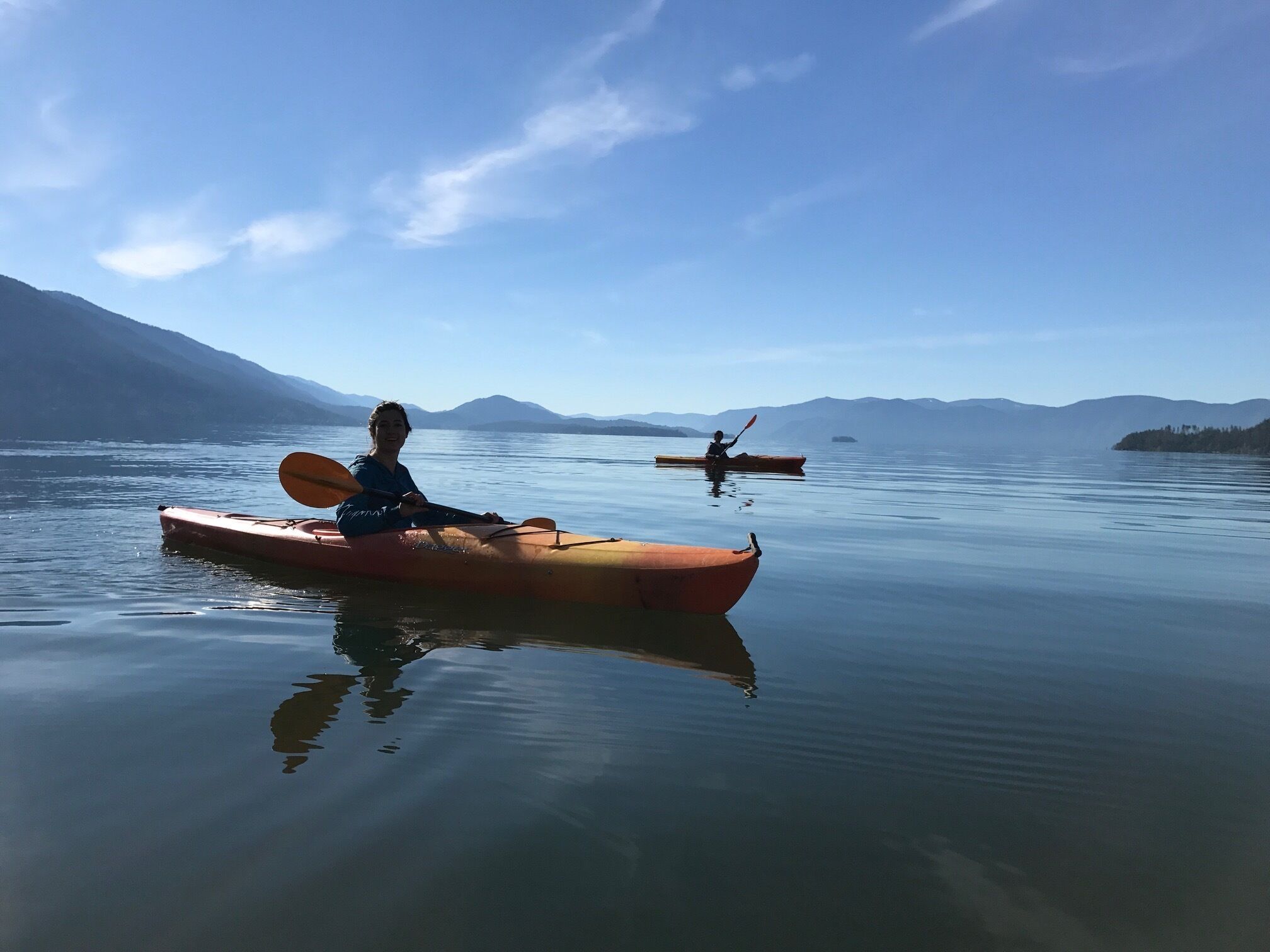 A calm lake with kayaks and a distant mountain range.