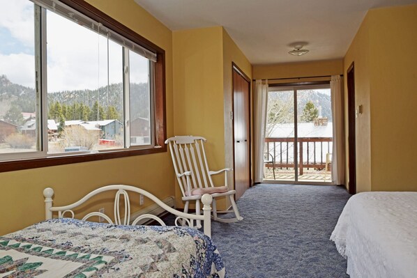 Une chambre à coucher avec un lit, un fauteuil à bascule et une vue sur un paysage enneigé, visible à travers une grande fenêtre.
