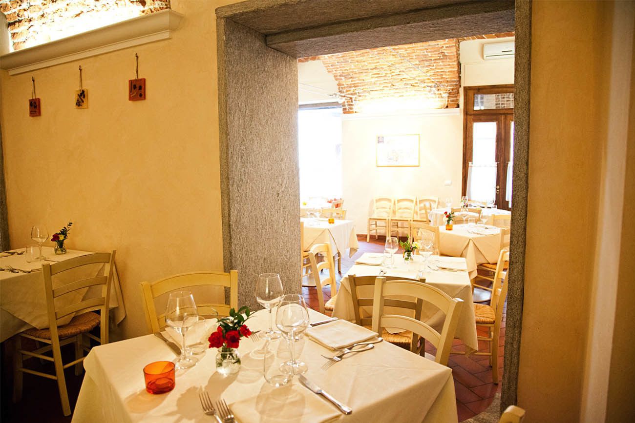 A dining area with tables set for two, each with a vase of red flowers, wine glasses, and cutlery.