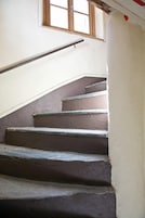 Una escalera con barandilla y un ventanal encima.