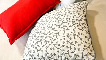 A bed with a white pillow featuring a black floral pattern and a red pillow.