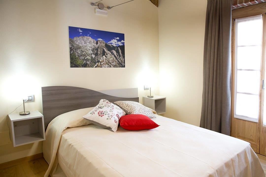 Ein Schlafzimmer mit Bett, Nachttisch, Wandlampe und einem Fenster mit Vorhängen.