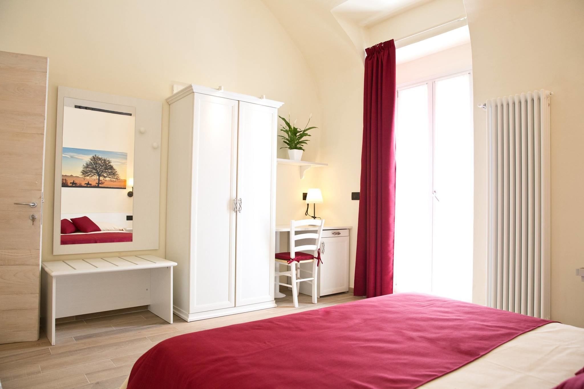A bedroom with a bed, a desk, a chair, a wardrobe, and a window with curtains.