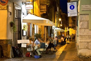 Un café al aire libre con mesas y sillas, un letrero que dice 'Osteria Senza Fretta' y una señal de zona peatonal.