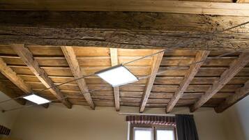 A room with exposed wooden beams, a window with curtains, and a painting on the wall.