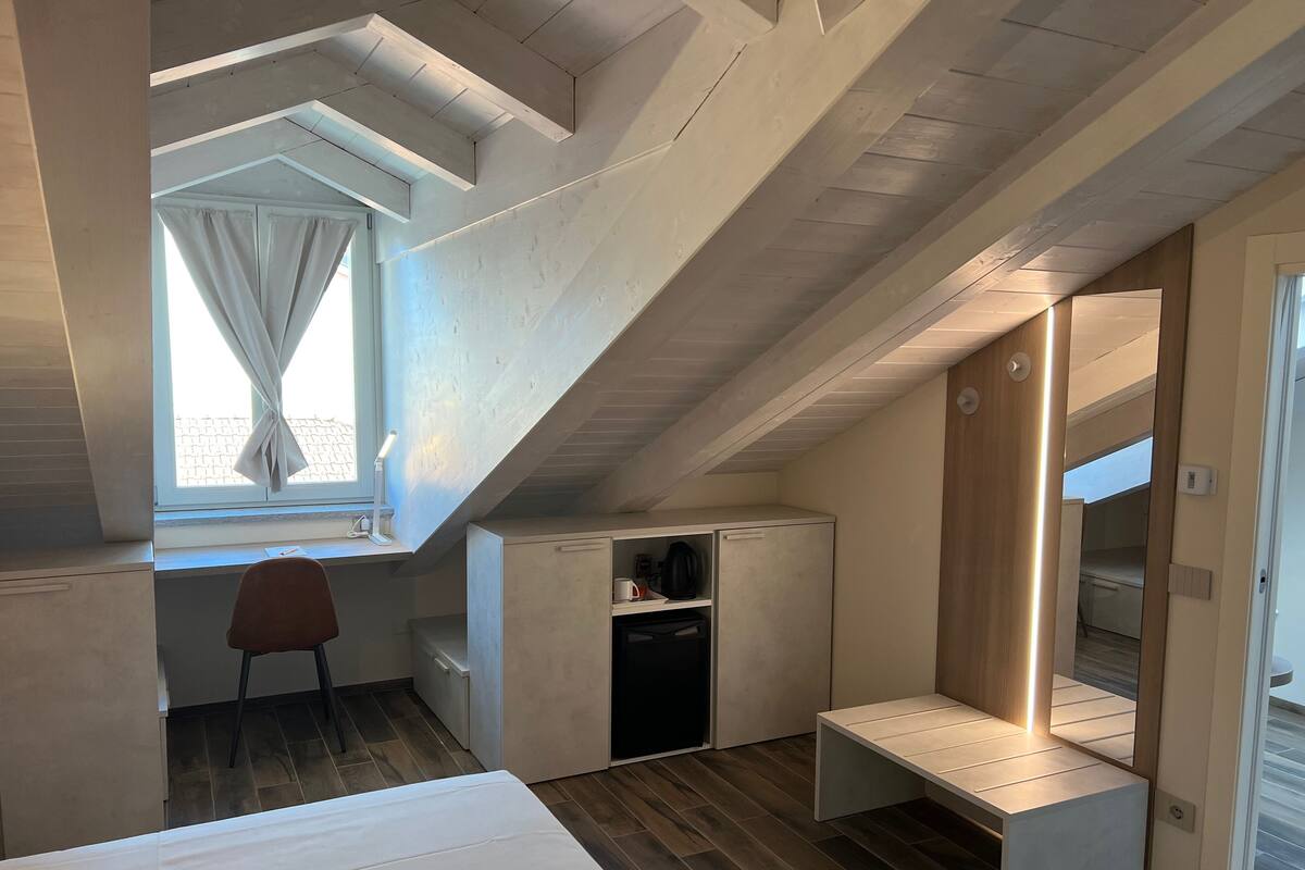 A compact, modern room with a sloped ceiling, a desk with a chair, a bed, and a built-in bench.