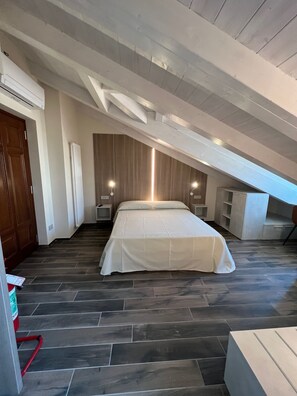 A bedroom with a sloped ceiling, a bed with a white bedspread, a wooden headboard, two bedside lamps, a radiator, and a small white nightstand. - Osteria Senza Fretta Affittacamere (Cuneo)