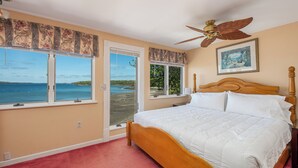 Une chambre avec un grand lit, un ventilateur de plafond et une vue sur la plage par les fenêtres.
