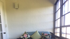 Ein Eckzimmer mit einem blauen Sofa, floralen Kissen, einem kleinen Tisch und einem Sessel.
