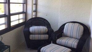 Ein Zimmer mit zwei Korbstühlen mit Streifenpolstern, einem kleinen Tisch und einem Fenster mit Jalousien.