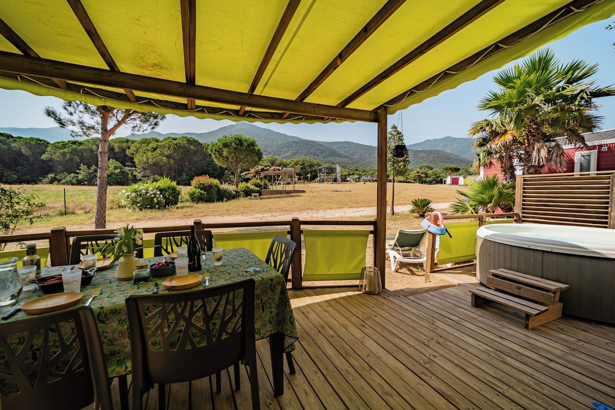 Un área de comedor al aire libre, techada, con una mesa dispuesta para dos, con vistas a un paisaje pintoresco de montañas y árboles.