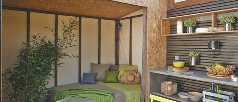 A cozy room with a bed, a dining table, and a shelf with plants and kitchenware.