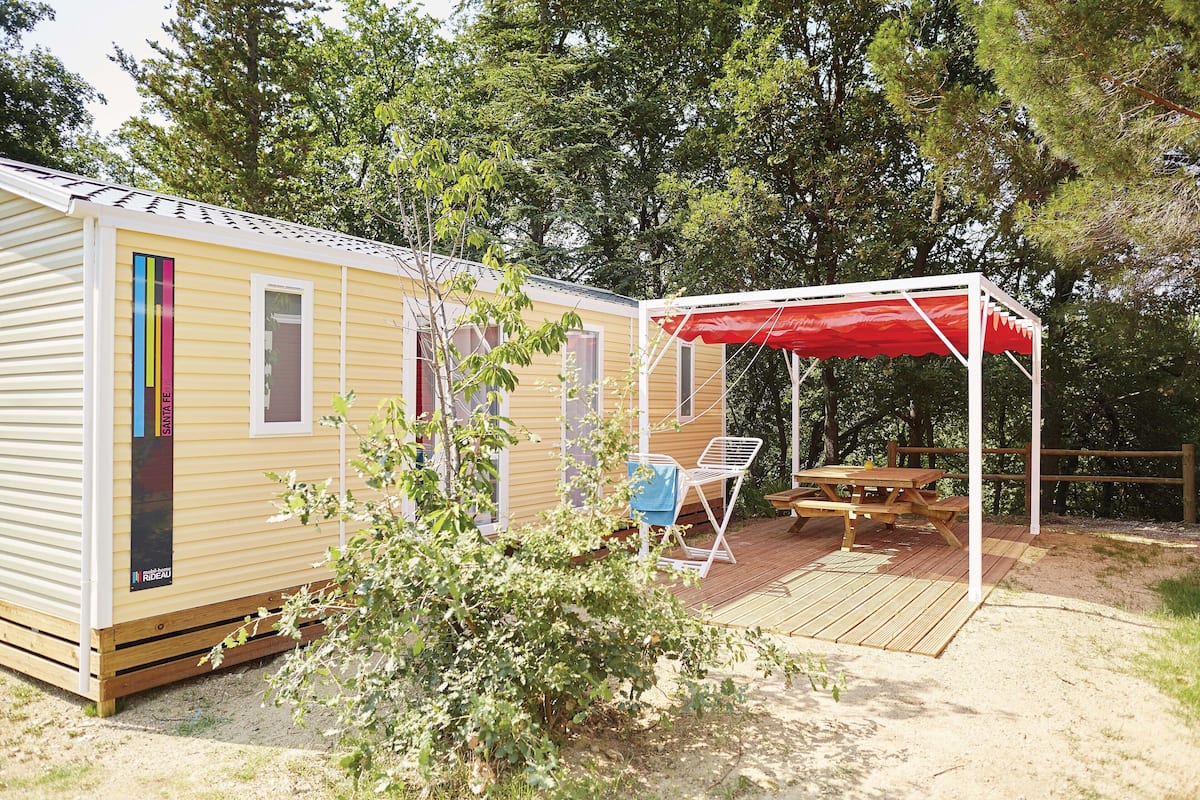 Una casa móvil con un porche, una mesa de picnic y un toldo rojo.