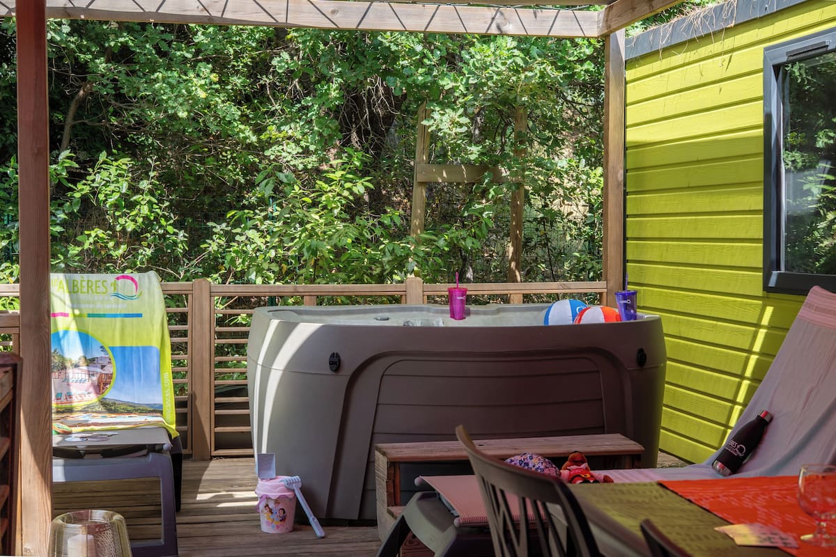 Un espacio exterior cubierto con jacuzzi, terraza de madera y una mesa con sillas.