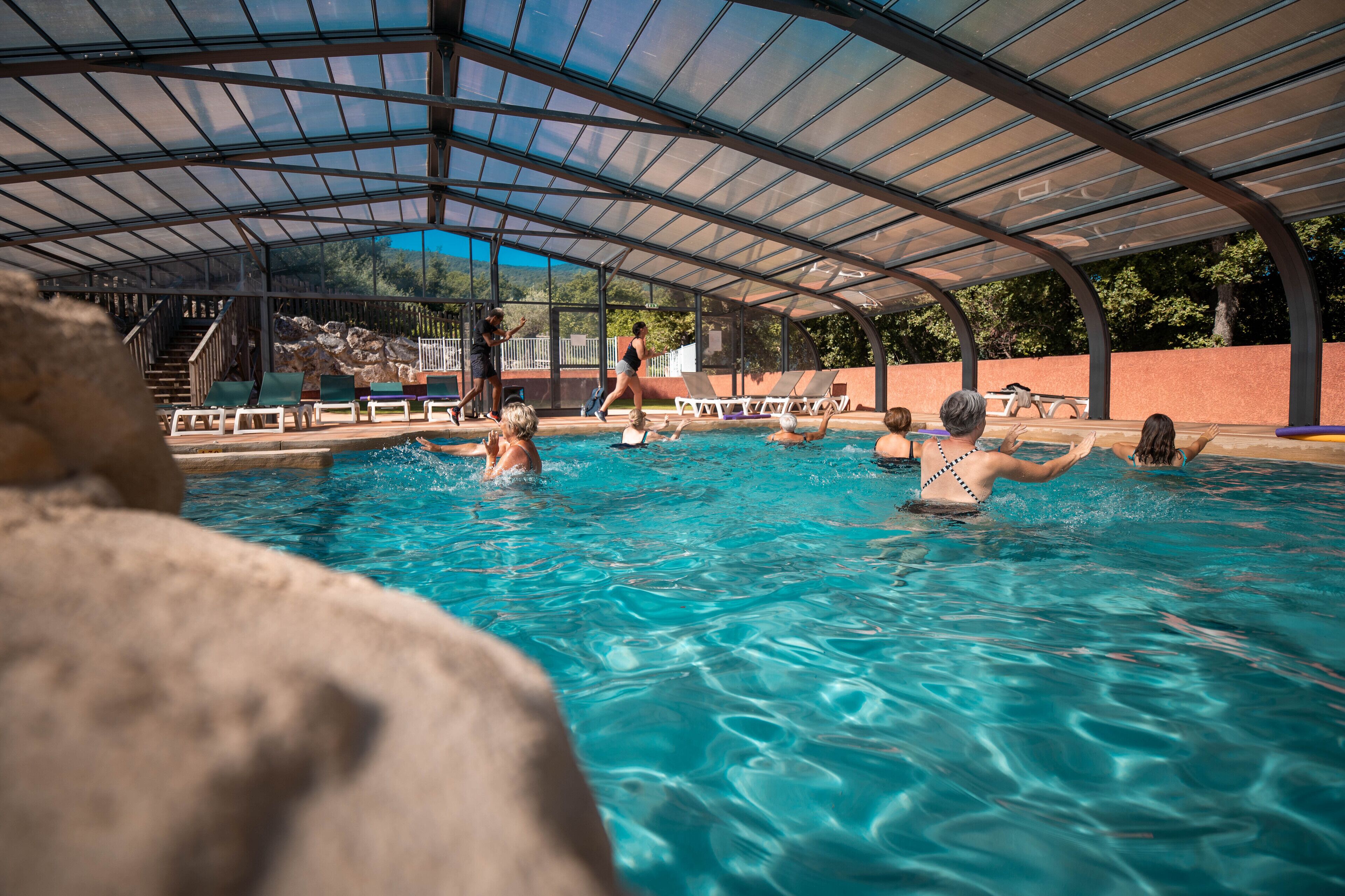 Une piscine dotée d’un toit en verre, entourée de chaises longues et d’un mur en pierre.