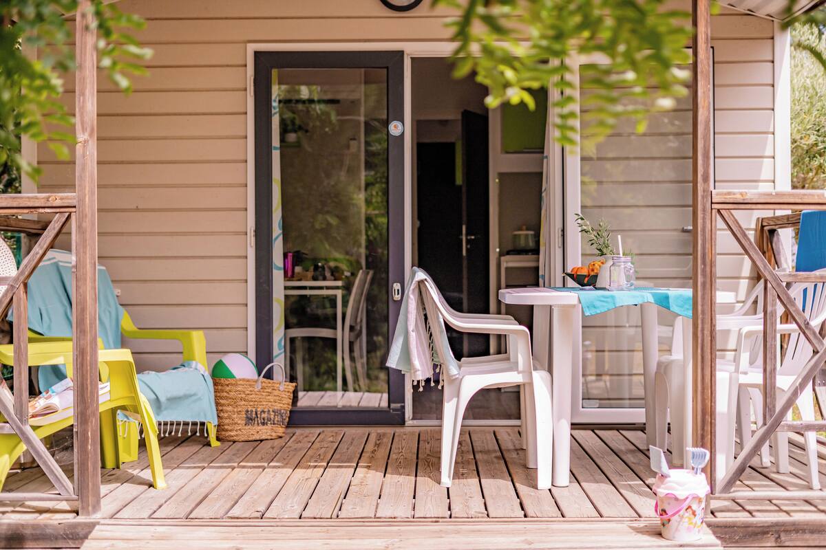 Una terraza de madera con mobiliario exterior, incluyendo sillas y una mesa, y una cesta en el suelo.