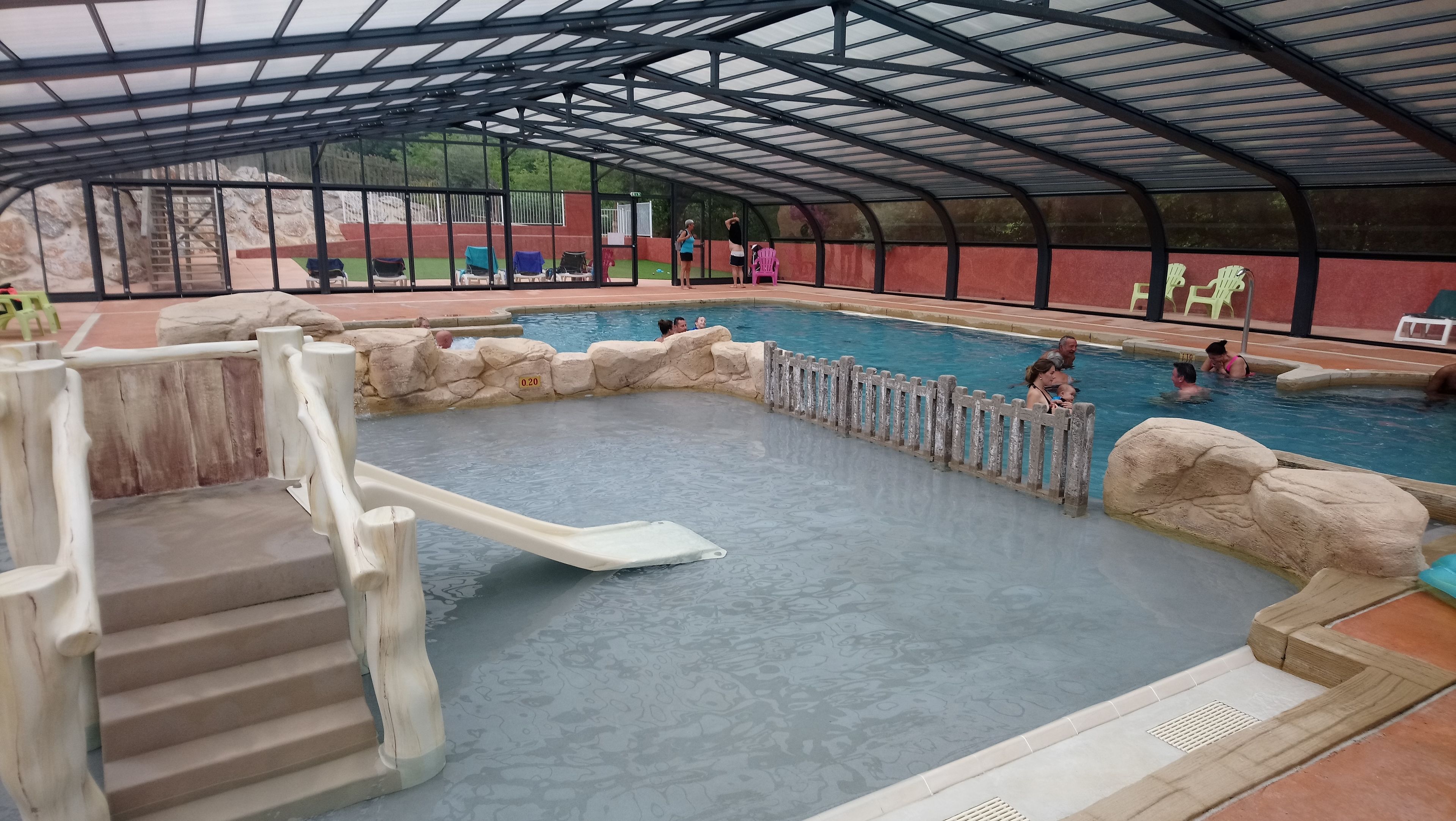 An indoor swimming pool with a covered area, stone walls, and a wooden deck.