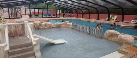 An indoor swimming pool with a covered area, stone walls, and a wooden deck.
