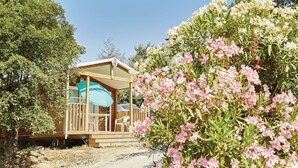 Une cabane en bois dotée d’un porche couvert, de meubles d’extérieur et offrant une vue sur un jardin parsemé de fleurs roses.