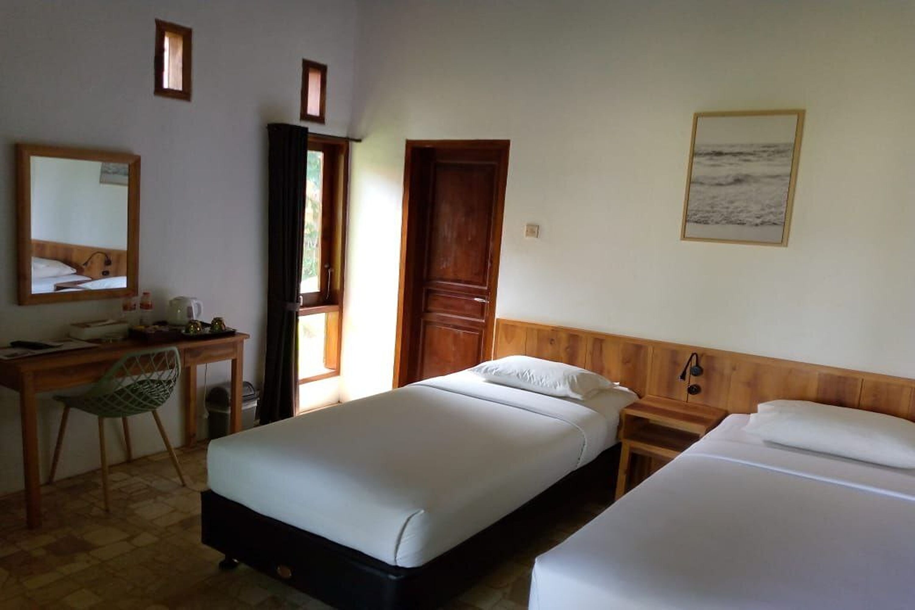 A hotel room with a bed, a desk with a chair, a wooden door, and a framed picture on the wall.