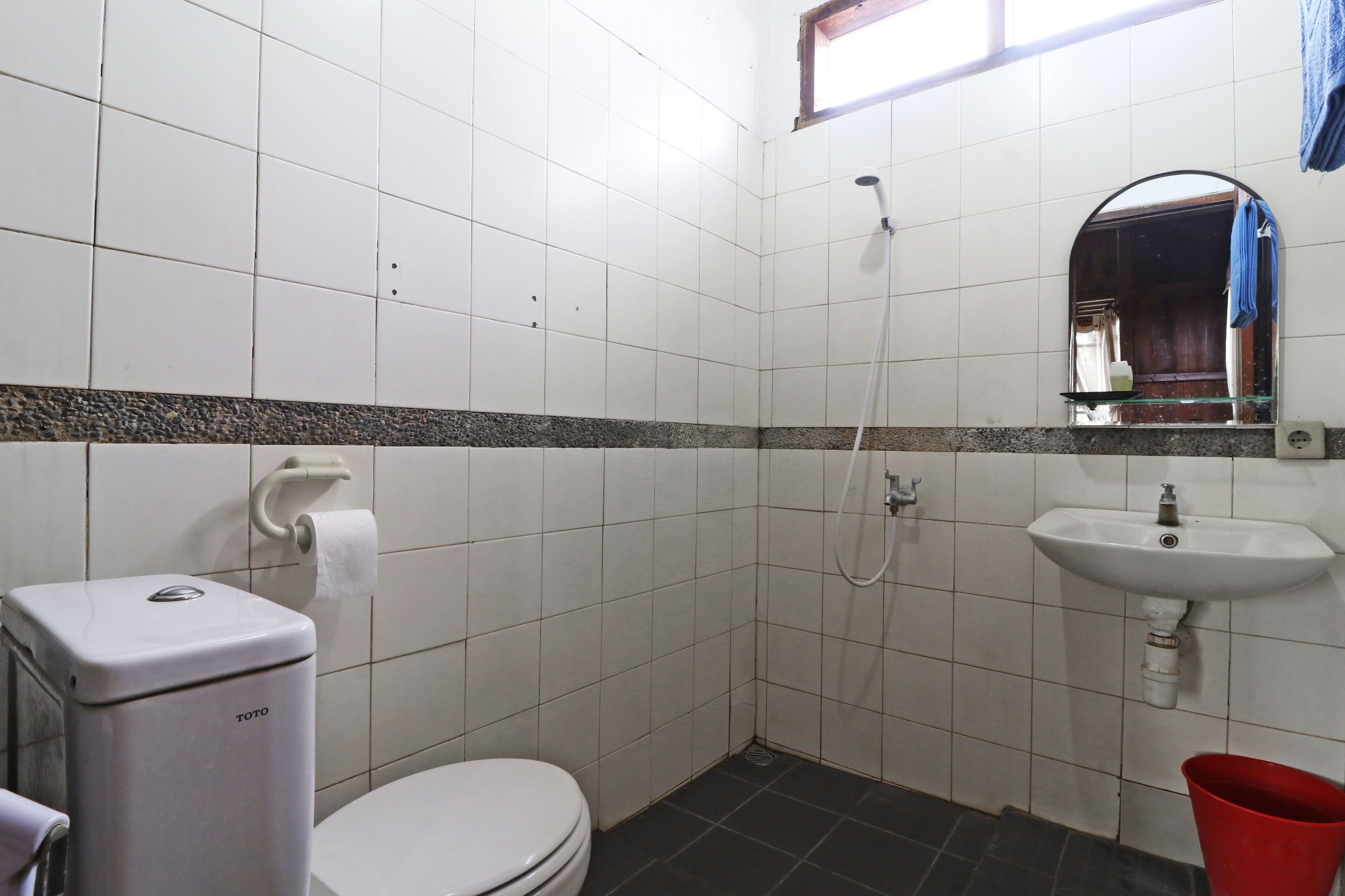 A small bathroom with white tiles, a white toilet, a sink, and a shower.