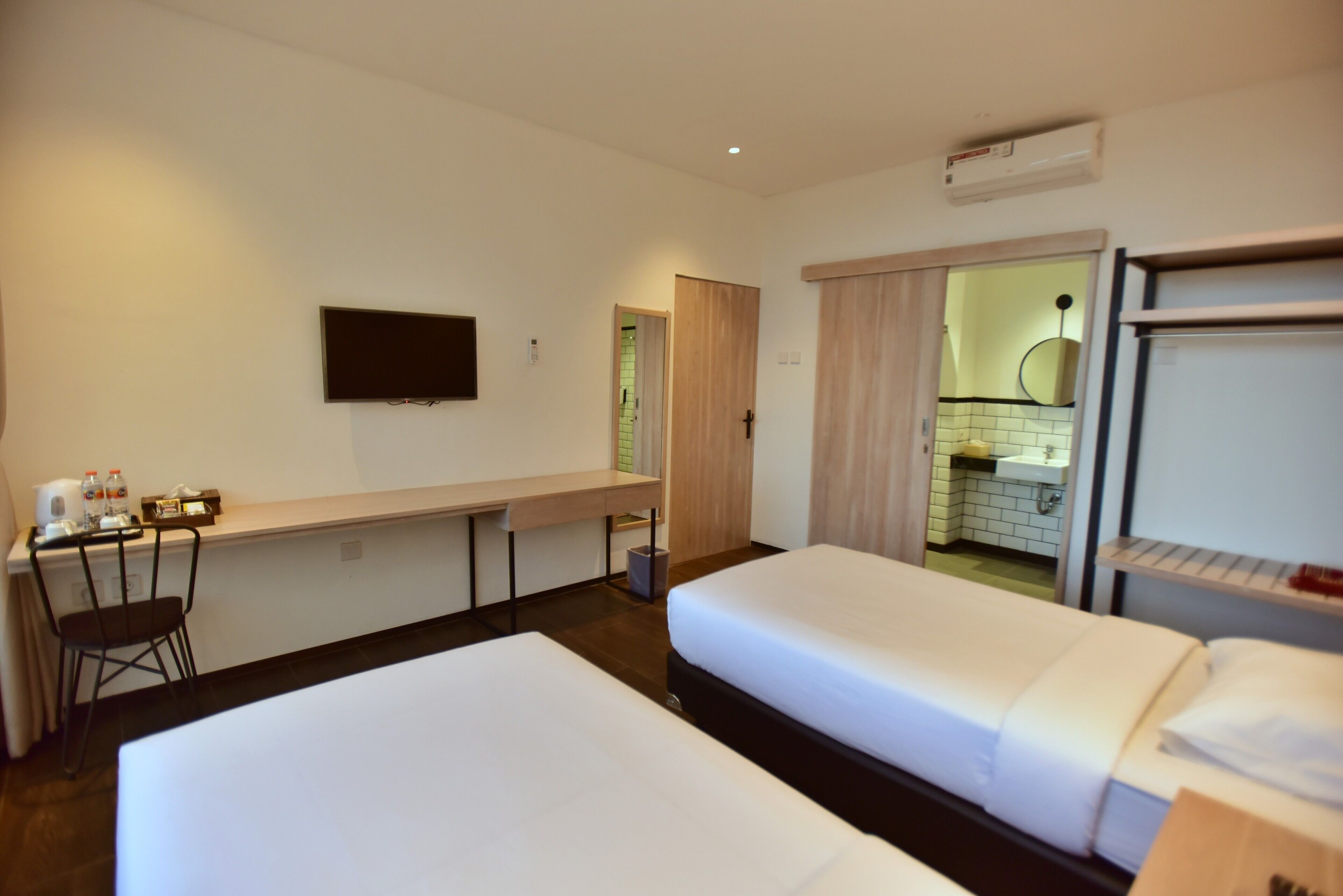 A hotel room with two beds, a desk with a chair, a TV, and a bathroom visible through an open door.