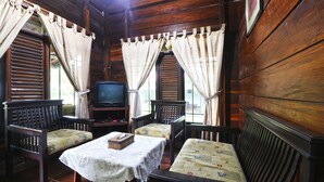 Eine Holzhütte mit Fernseher, zwei Holzstühlen, einem Tisch mit Spitze und Vorhängen.