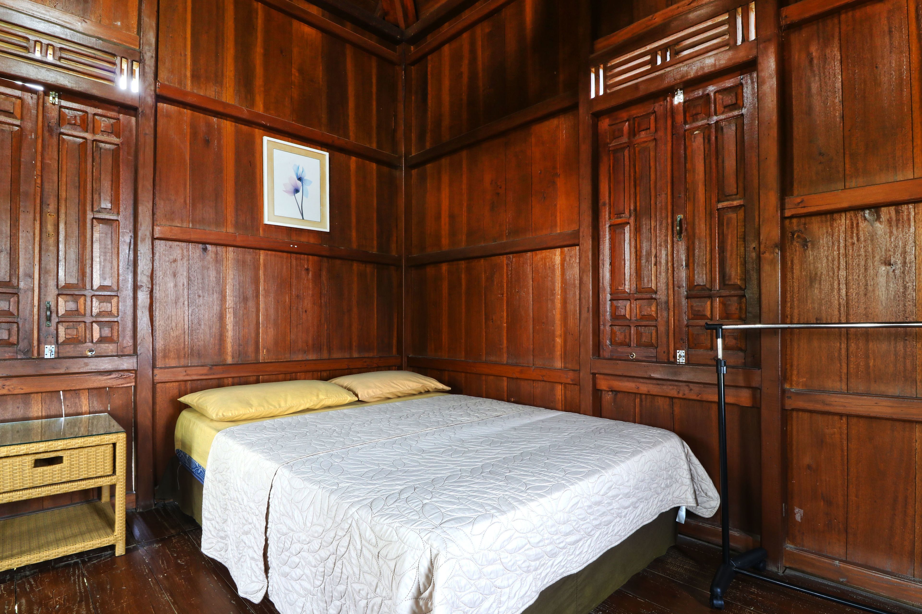Een kamer met houten lambrisering, een bed, een tafeltje en een foto aan de muur.