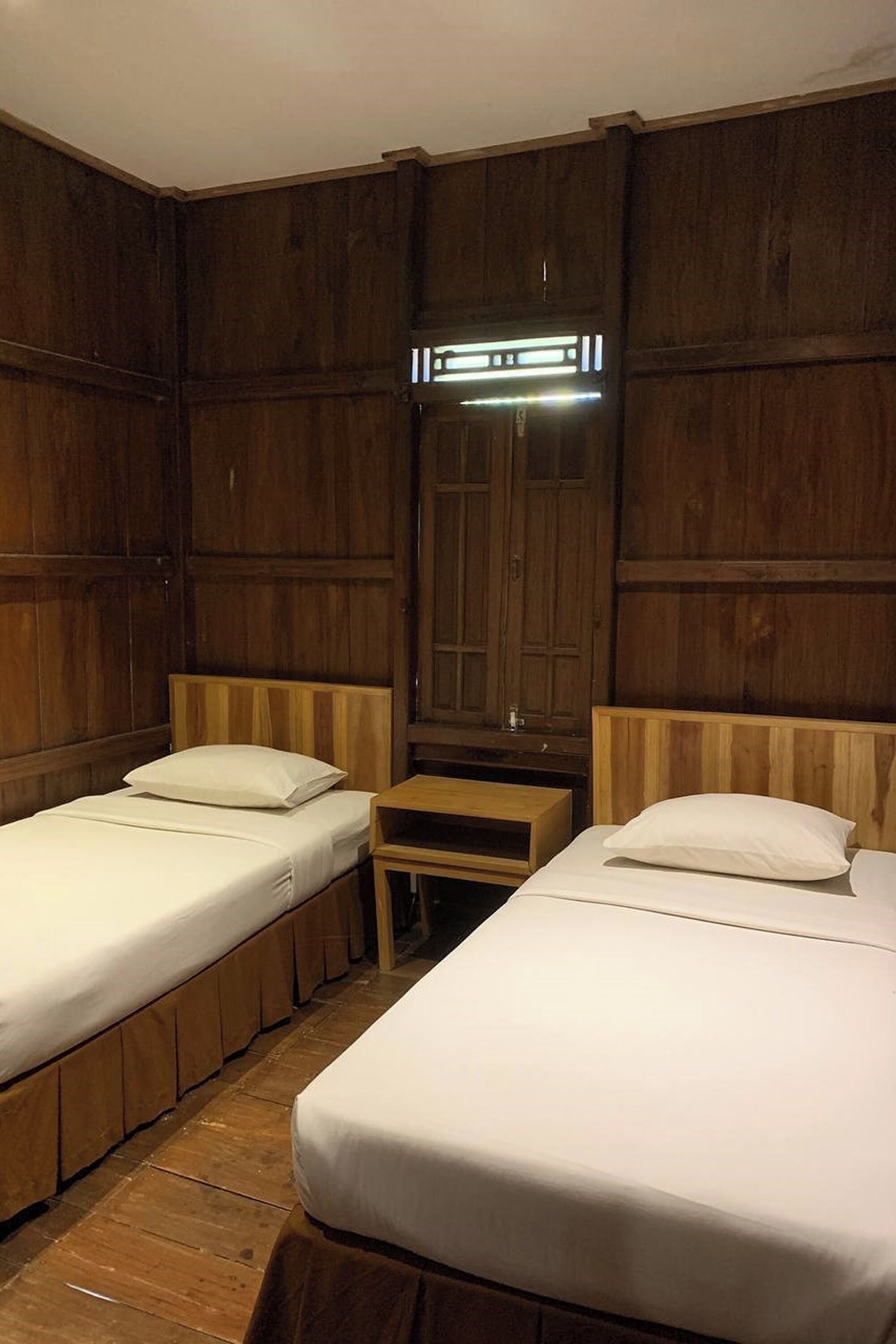 Une chambre avec deux lits simples, des lambris en bois sur les murs, une petite table de chevet et un miroir au-dessus de la tête de lit.