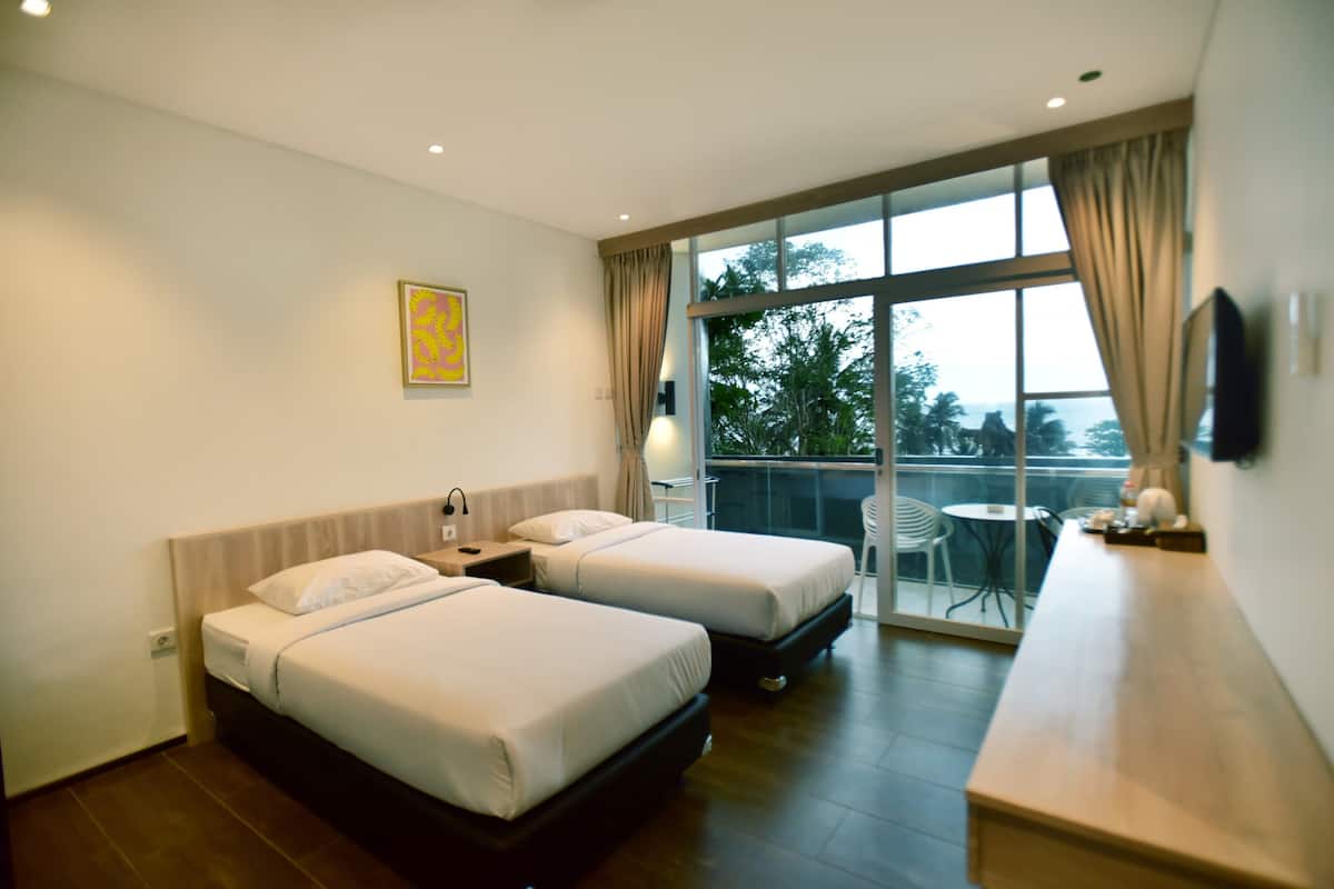 Habitación de hotel con dos camas, un balcón con vistas y una pequeña mesa.