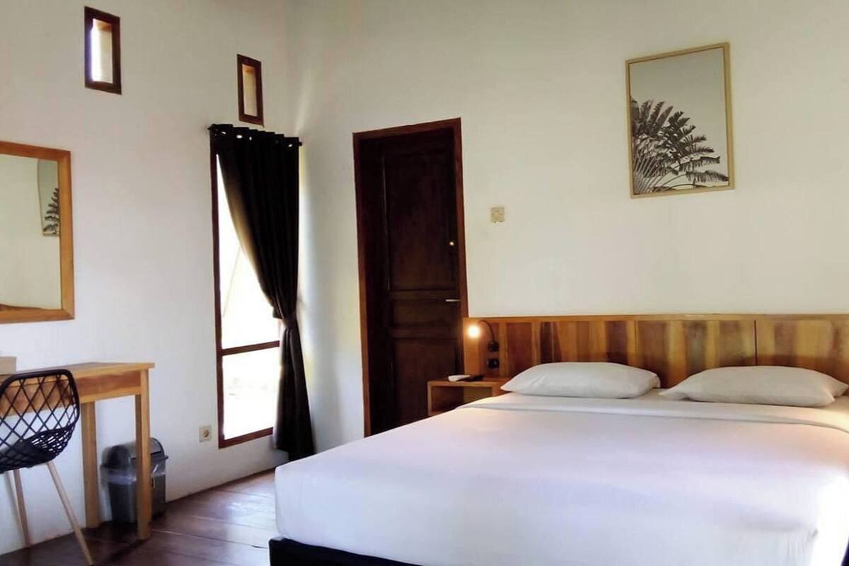 Un dormitorio con cama, escritorio, silla, puerta y un cuadro colgado en la pared.