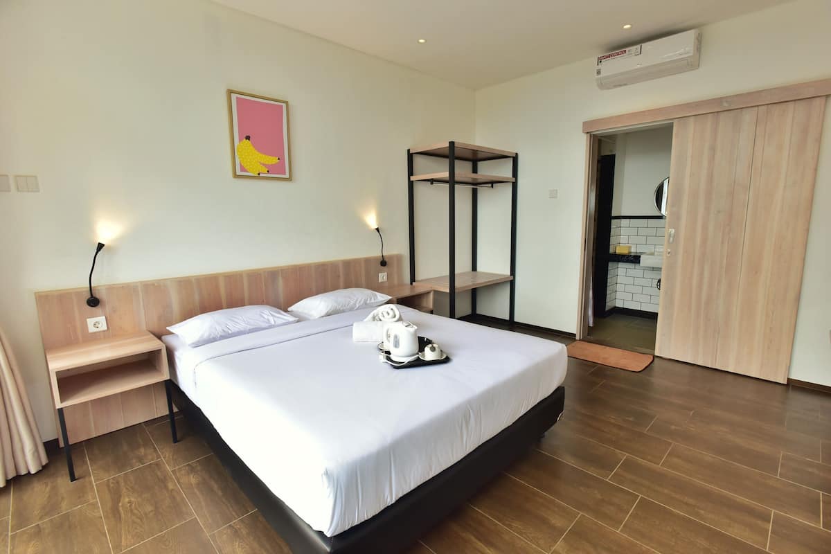 Una habitación de hotel con una cama, mesitas de noche, un armario y un baño visible a través de una puerta abierta.