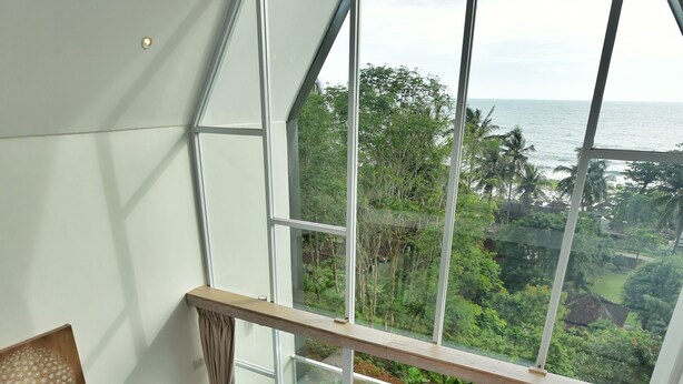 Ein Schlafzimmer mit einem großen Bett, einem Holztisch und einem Balkon mit Blick auf das Meer und Grünflächen.
