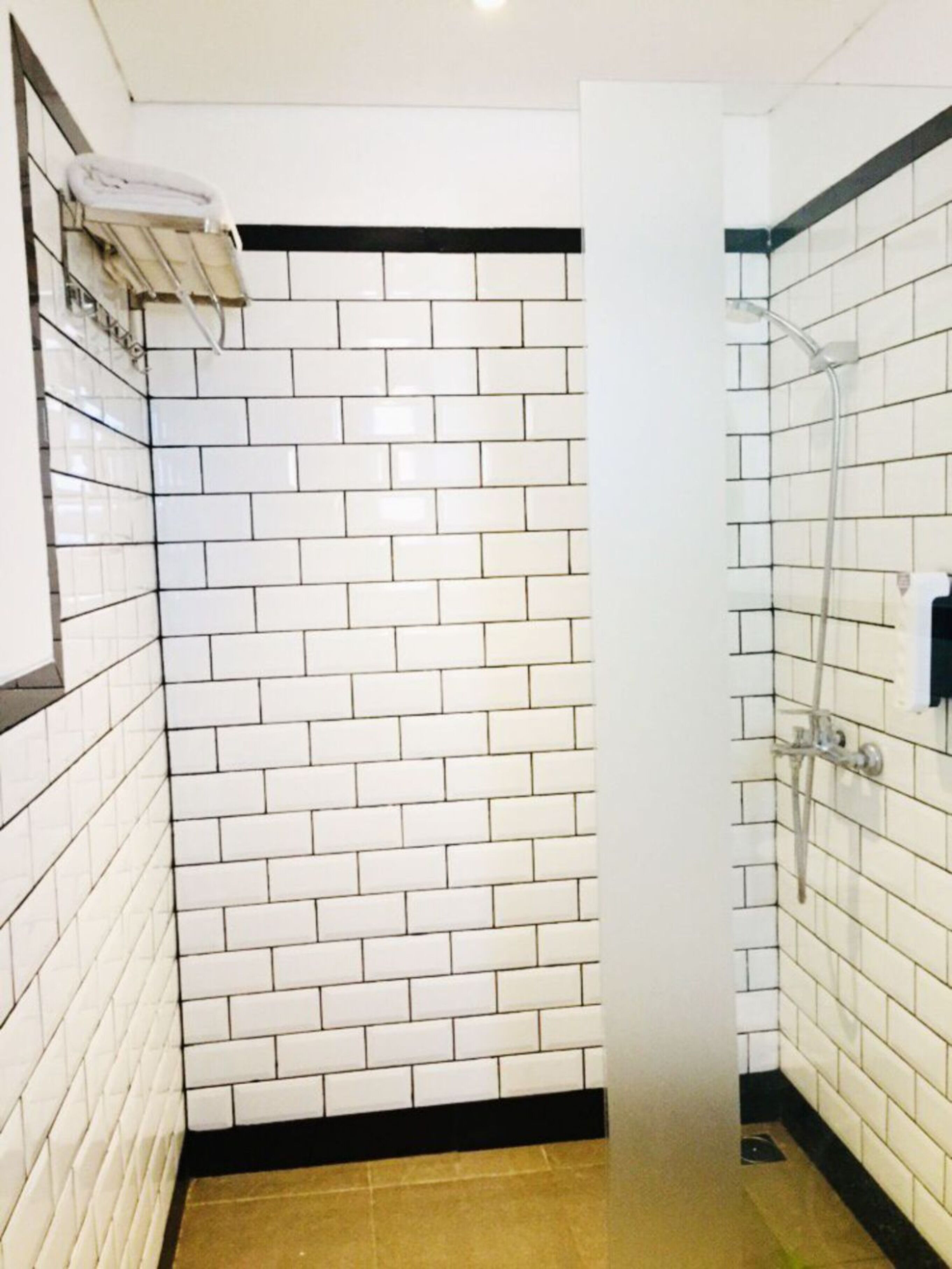 Un baño con azulejos blancos tipo metro, zócalo negro y ducha con puerta de vidrio.