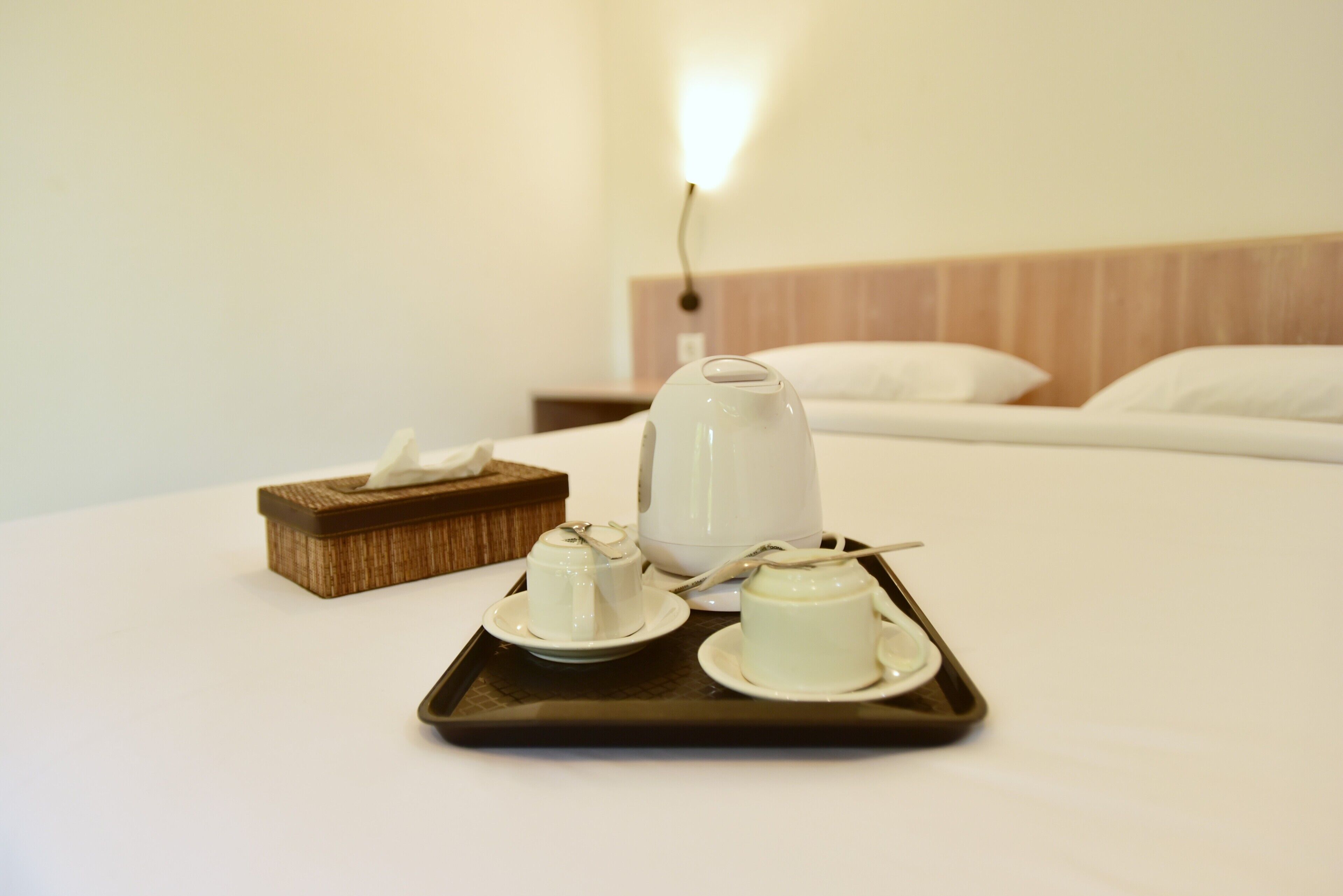 Un lit bien fait, avec un plateau contenant des tasses à thé et une théière, posé sur une table dans une chambre d’hôtel.