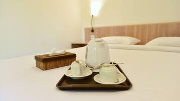 Una cama bien hecha con una bandeja de tazas de té y una tetera sobre una mesa de habitación de hotel.