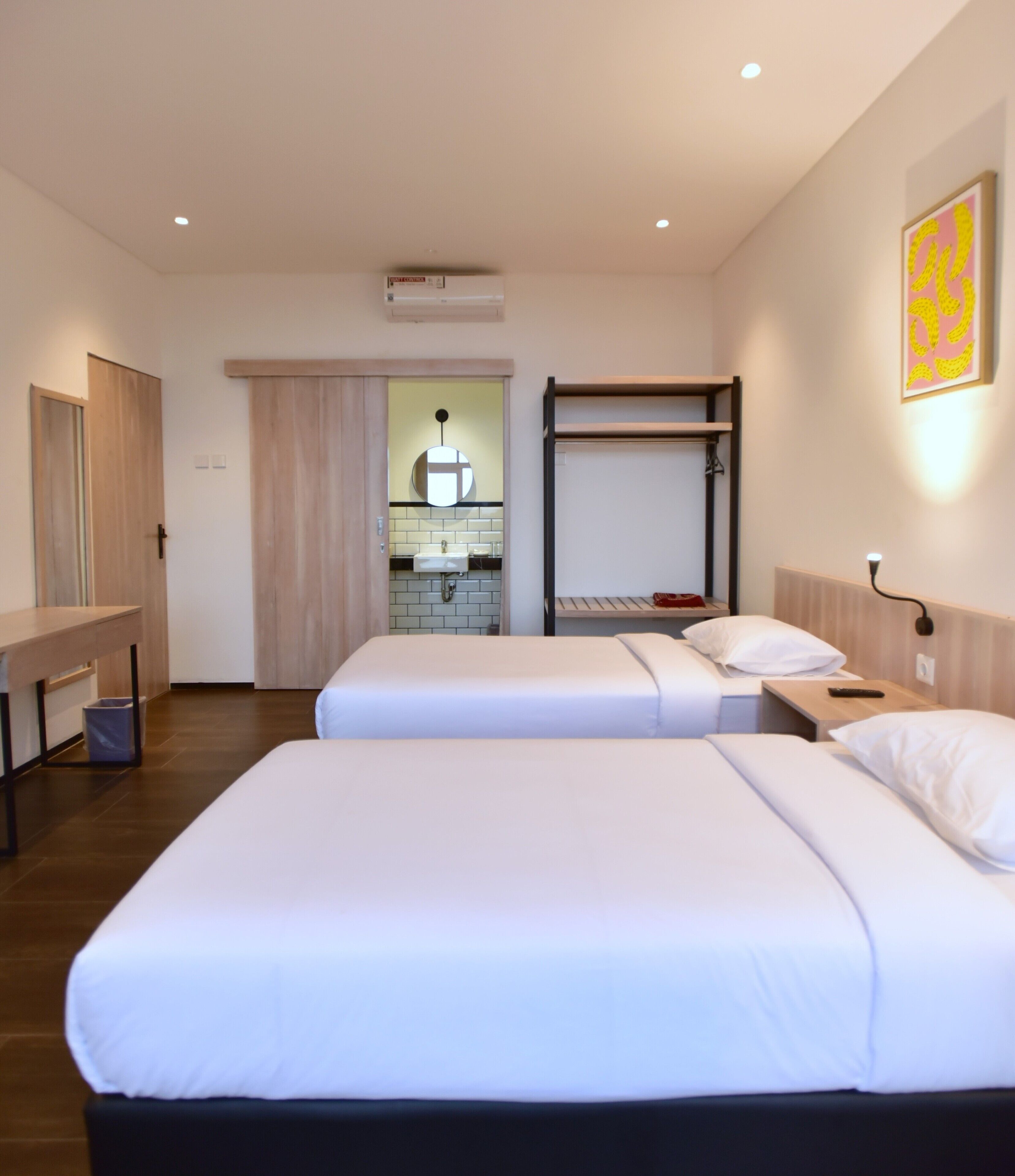 A hotel room with two beds, a small kitchenette, and a bathroom.