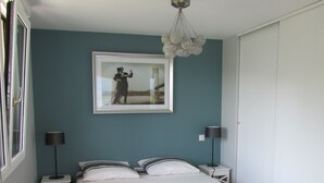 A bedroom with a bed, two bedside tables, a standing lamp, a framed picture on the wall, and a window with blinds.